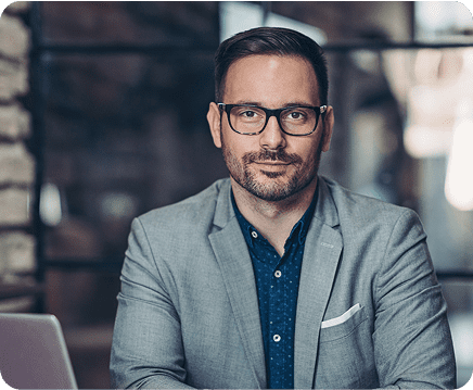 T4T Mentory - home de blaser cinza e oculos, em mesa de trabalho, como se estivesse conversando com alguém a sua frente.